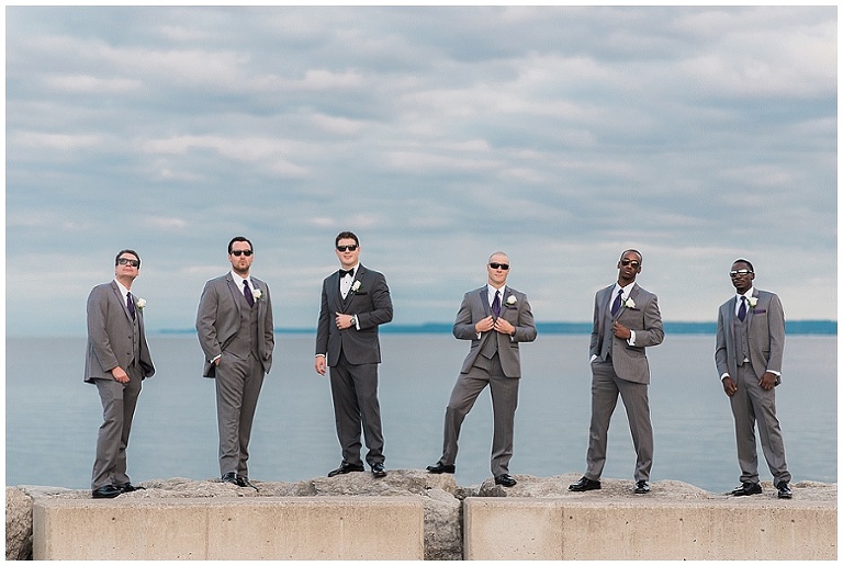 Groomsmen pose on rocks along waterfront at Burlington wedding venue