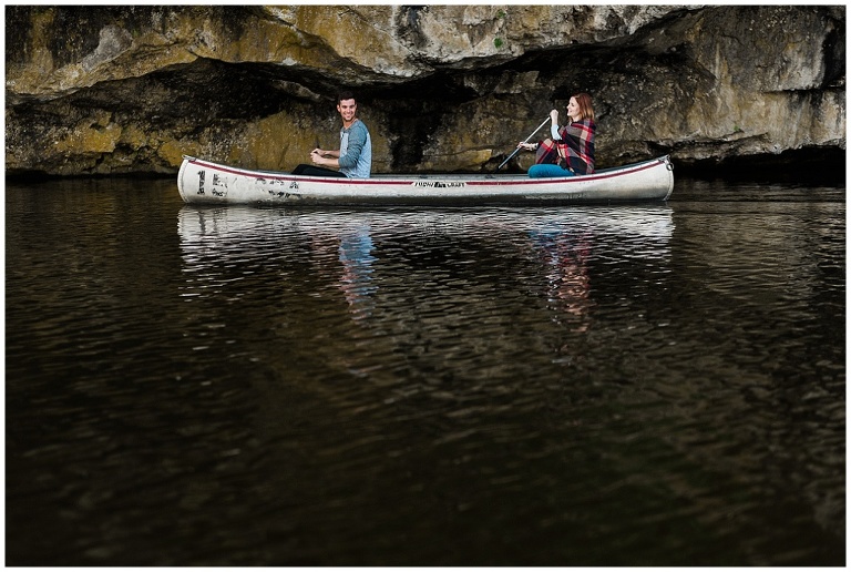 Couple paddles in canoe on lake under rocks at conservation area