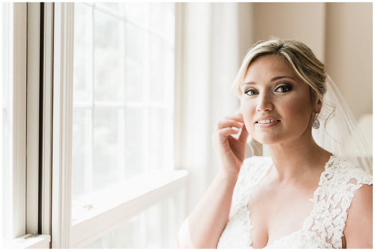Bride looking straight into camera on her wedding day as she places her earring on her ear