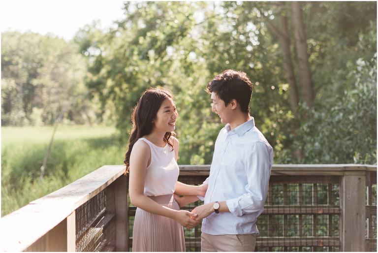 A couple hold each others hands on a wooden lookout in a marsh