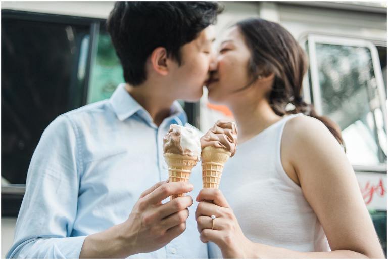 Couple holds ice cream cone, and they are kissing in the background slightly out of focus at Jack Darling Park Mississauga