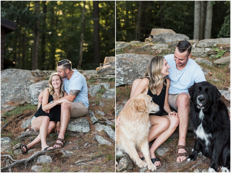 Man and woman sitting on rocks and moss outside of their cottage with their golden retriever and black lab dogs