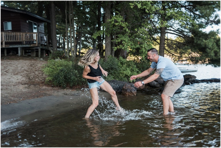 Man and woman splashing water at each other at their cottage during their engagement session