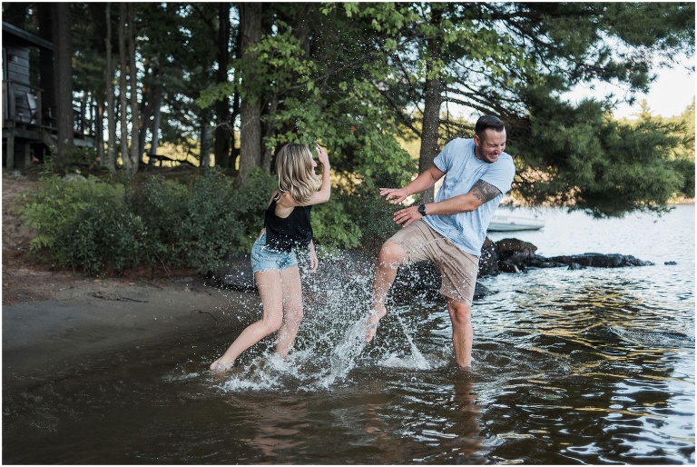 Man and woman splashing water at each other at their cottage engagement session.