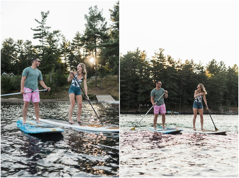 Man and woman paddleboarding together on a lake during their Muskoka cottage engagement session. Golden light leaks through the trees behind them