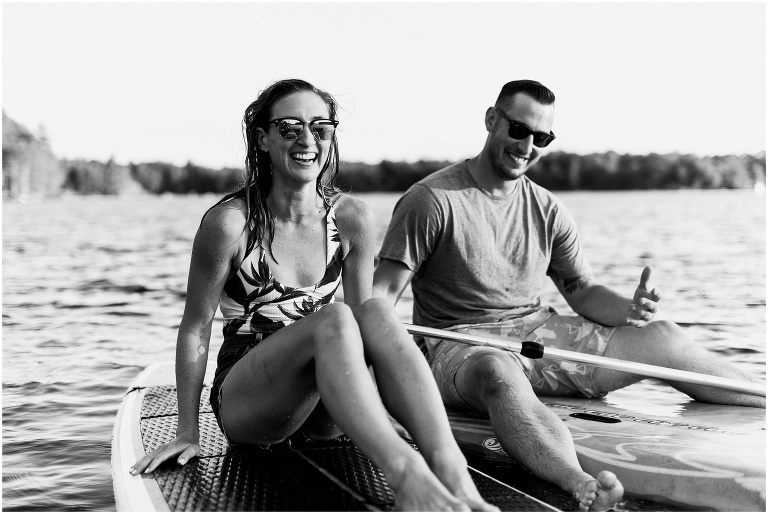 Black and white photograph of woman and man sitting on their individual paddle boards, and they are both smiling