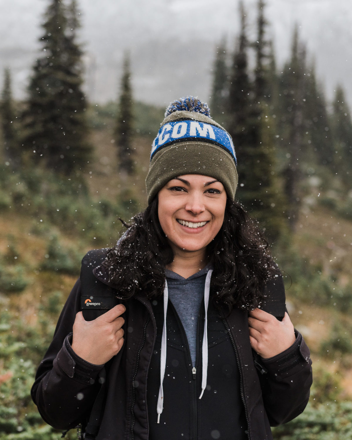 Caitlin Free hiking against Whistler Blackcomb while it's gently snowing, with toque on and LowPro backpack on