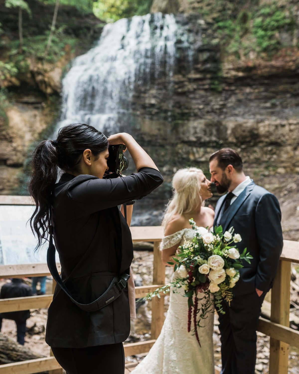 Photographer taking photo of bride and groom in front of a waterfall in Hamilton