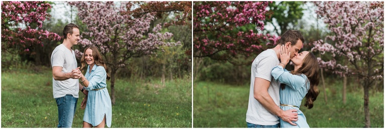 Newly engaged couple kissing passionately in front of apple blossoms during engagement session
