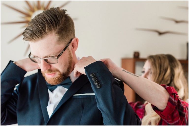 Bride adjusts groom's collar on his suit while they get ready together on their wedding day