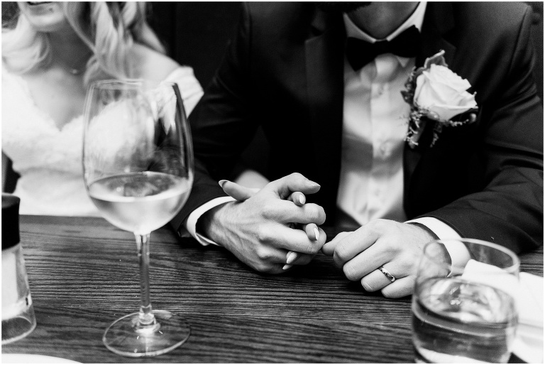 black and white photo of bride and groom holding hands on the dinner table at the Keg after they eloped