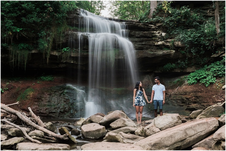 Couple holds hands for slow exposure photograph of smokey hollow waterfall in hamilton ontario