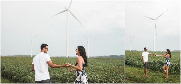 Couple holds hands and runs together in field in front of windmills in Dunnville Ontario for the engagement photos