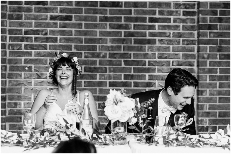Black and white photo of bride and groom laughing together at the head table during their wedding day at The Manor by Peter and Pauls