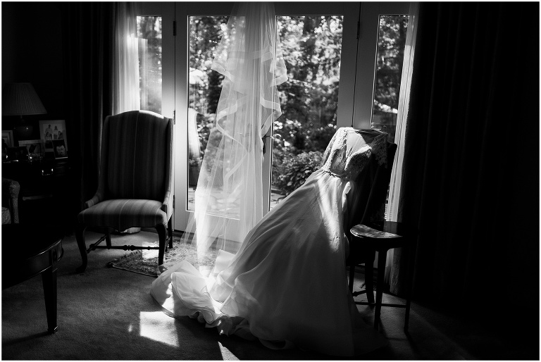 Black and white photo of wedding dress draped on chair in sunlight