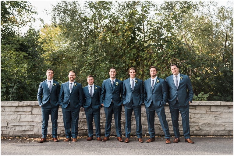 All groomsmen lined up along a stone bridge dressed in blue suits