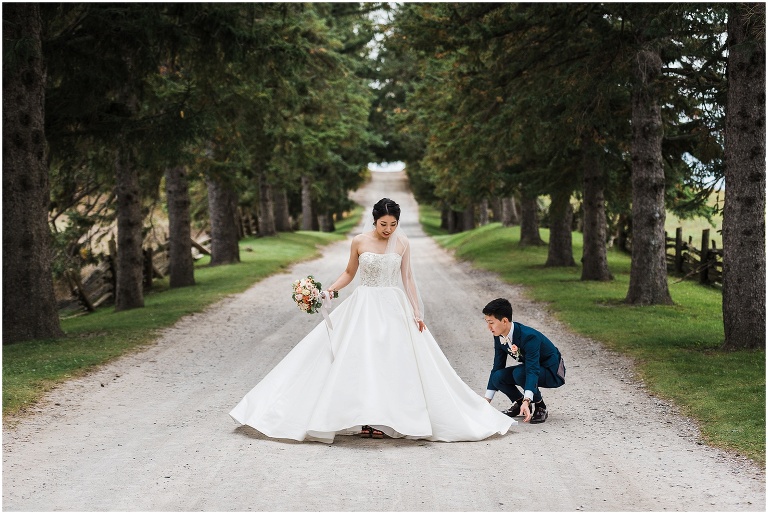 Groom helping his bride fan out her wedding dress on the road for a photo