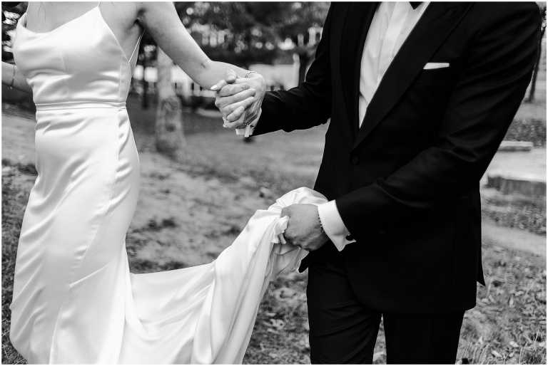 Close up of groom's hands holding bride's dress and her hand