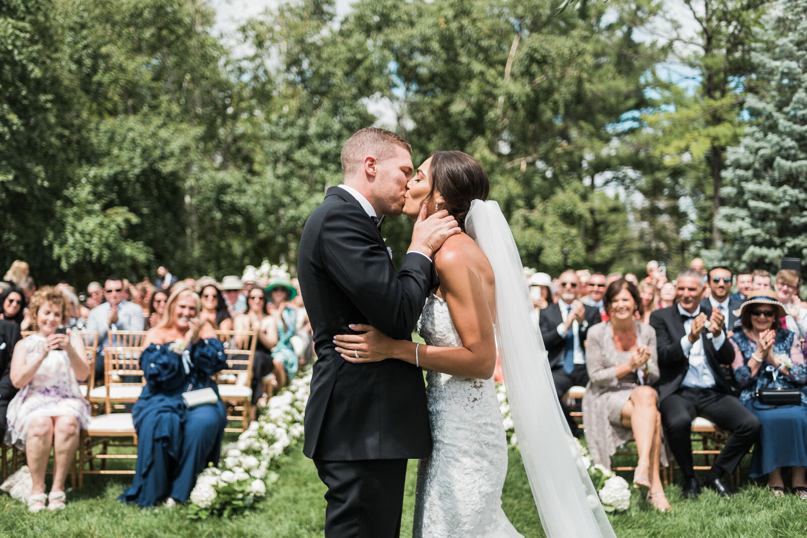Bride and groom kiss after saying I do on their wedding day with guests all behind them