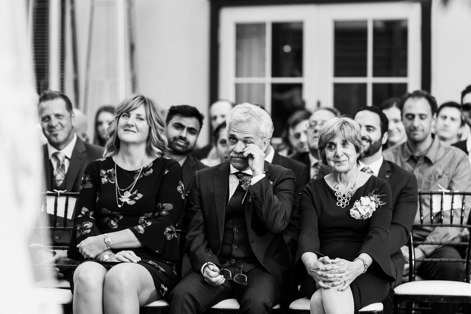 Groom's dad wiping a tear away as he watches his son get married