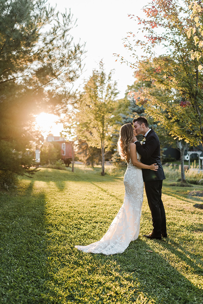 Bride and Groom facing each other kissing, while the sun sets behind at hem at Belcroft Estate