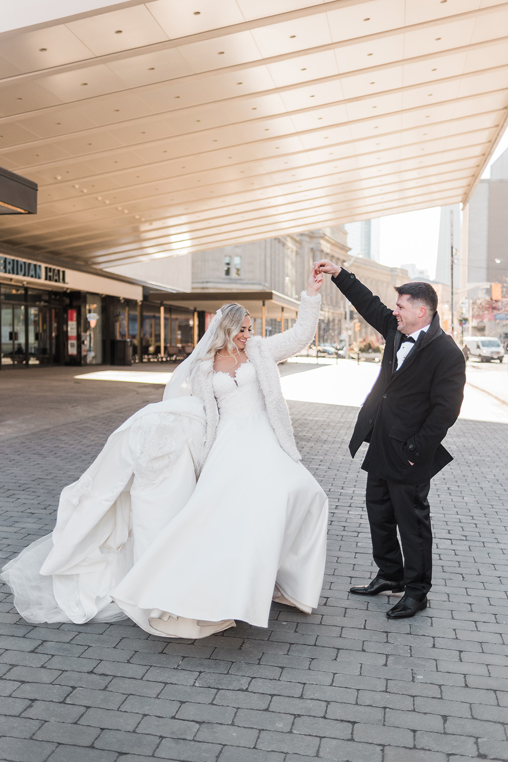 Bride and Groom spin under entranceMeridian Hall in Toronto, backlit by the sun