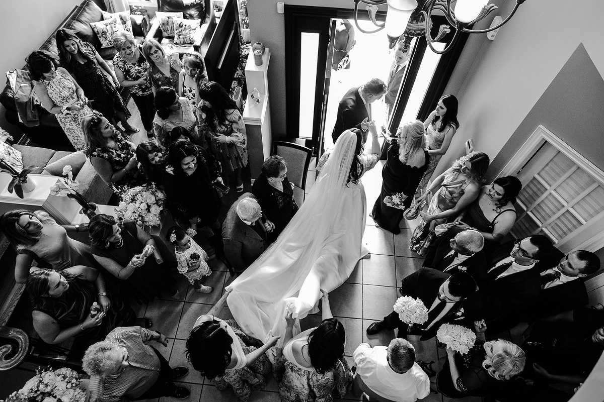 Overhead view of bride surrounded by thirty plus family members as her father leads her out the front door to her wedding at Guild Inn Estate in Toronto