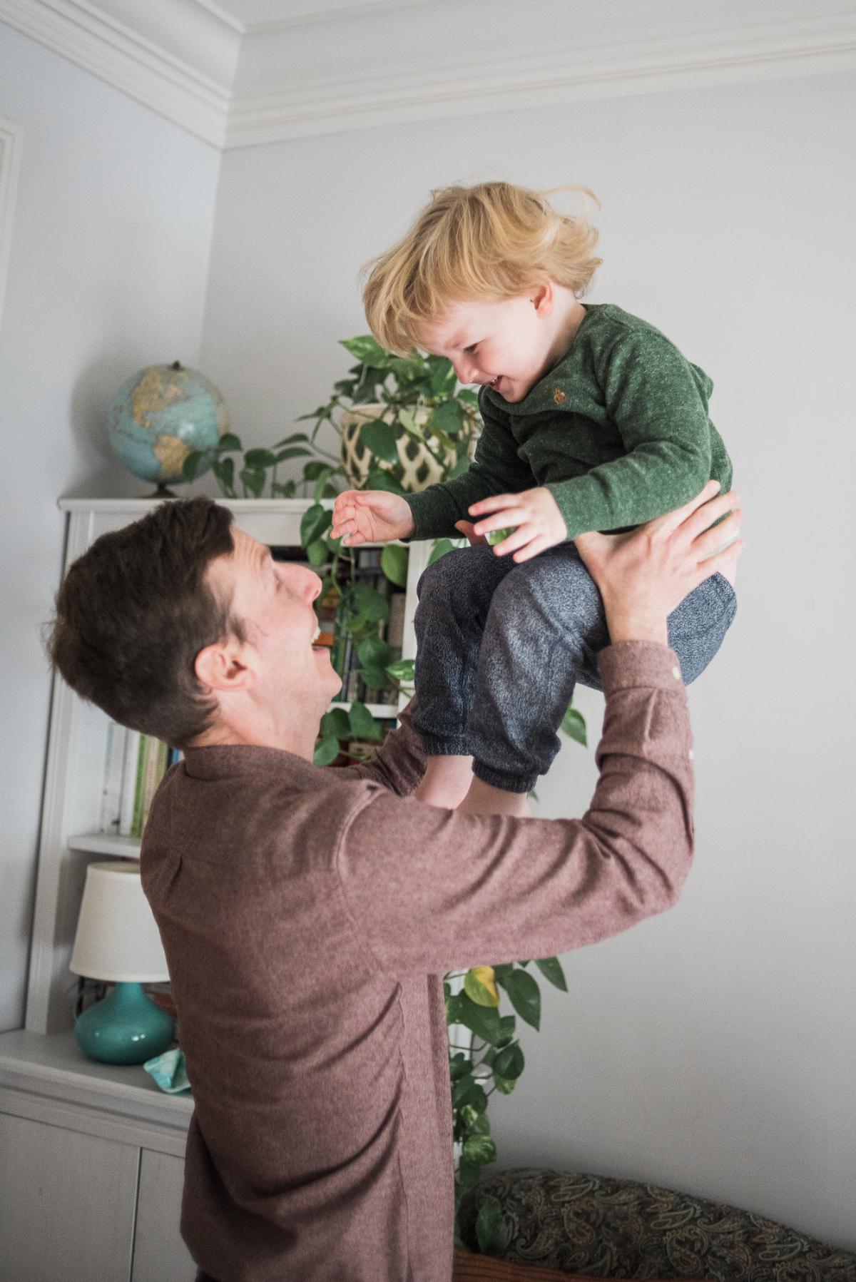 Dad throwing son up into the air inside their living room