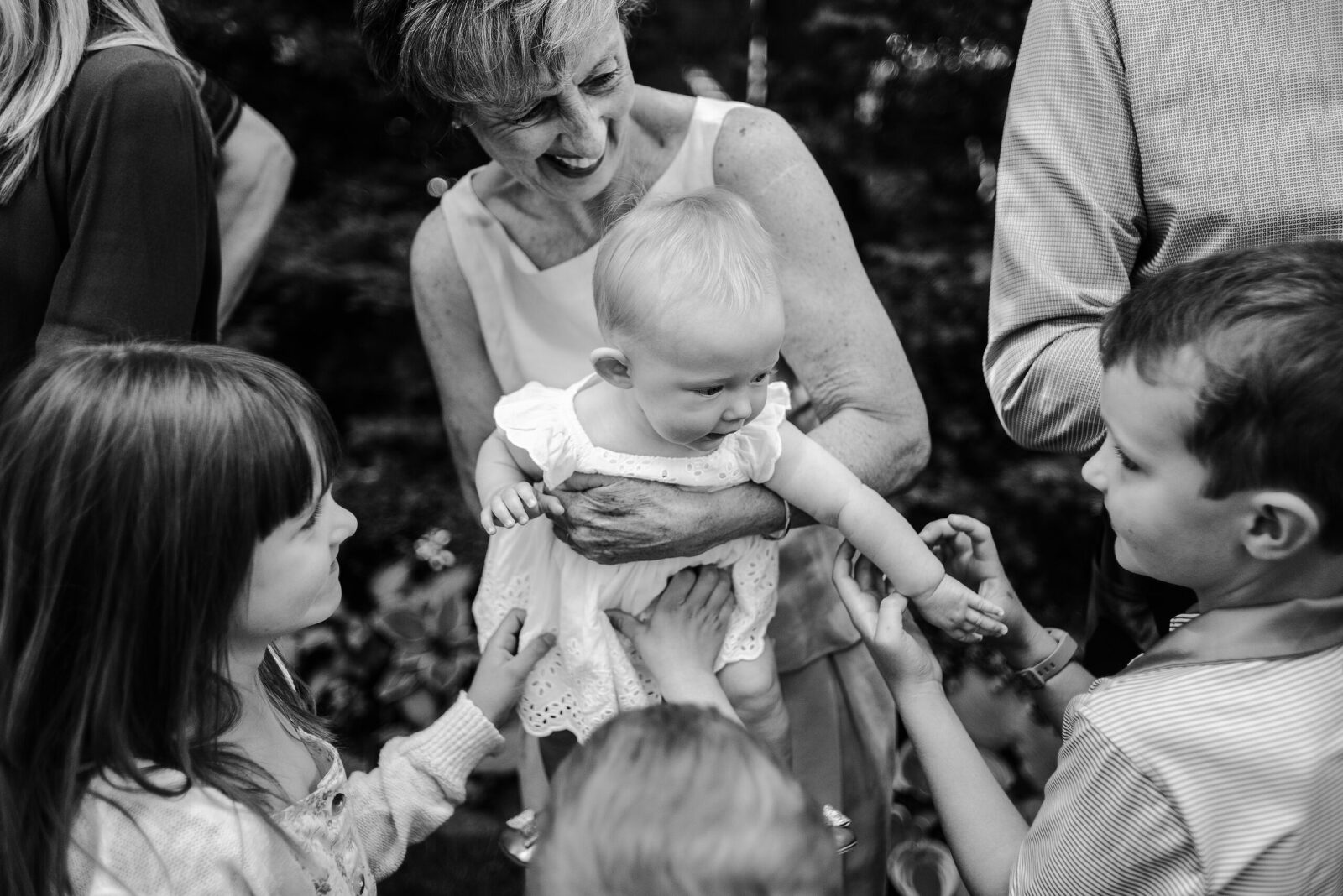 Grandmother holds infant granddaughter as cousins look at the infant