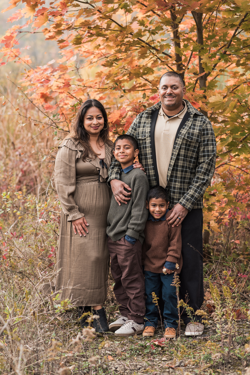 Family of four stands in front of colour changing trees in autumn all smiling