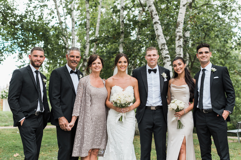 a group of 7 family members stand in a line together with the bride and groom in the center for their family photo at wedding