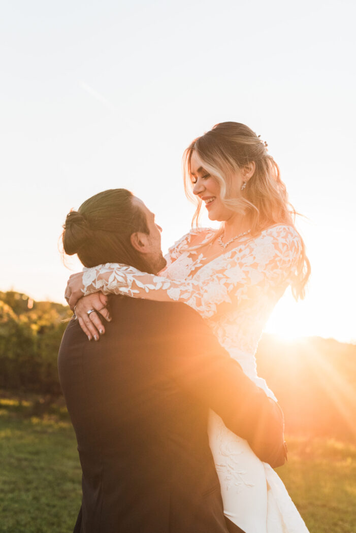 Bride being lifted by groom with golden sunsest light shining through them